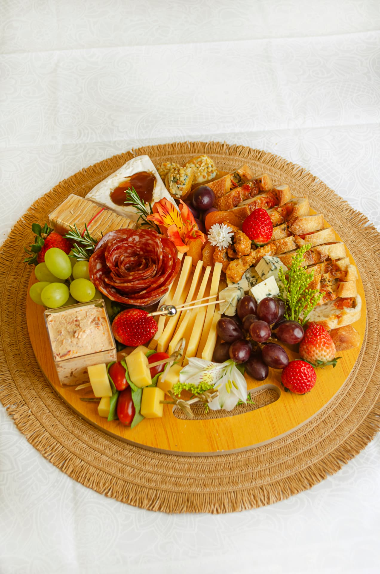 Tábua de charcutaria com queijos, flor de salame, patê, frutas e baguete.