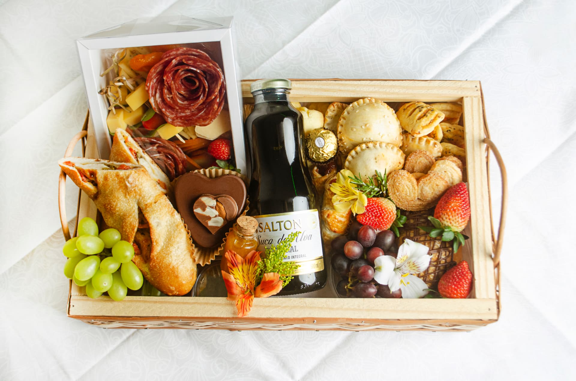 Cesta Café Completo em bandeja de vime com suco integral, salgados folhados, frios, frutas e doces.